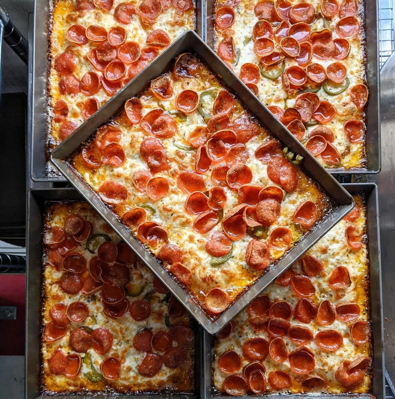 five pans of Detroit Deep Dish pizza stacked on a counter. 