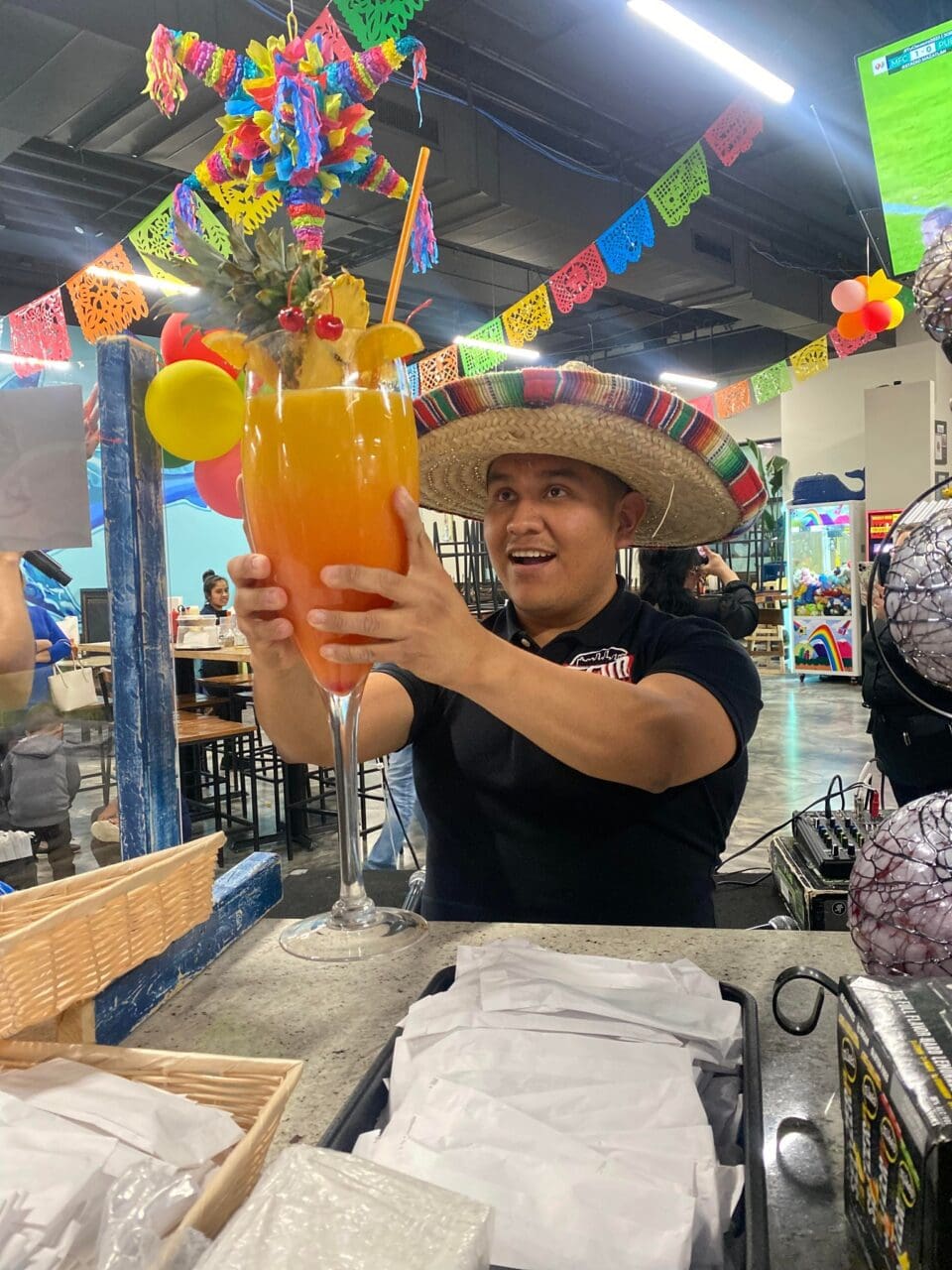 a man in a black shirt wearing a sombrero holding a large glass 