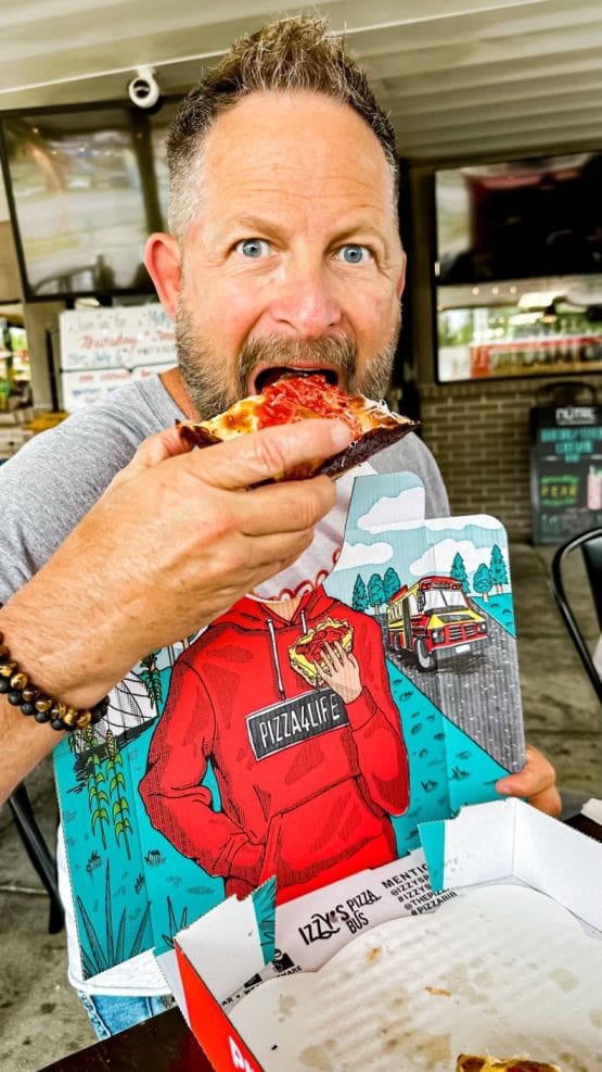 A handsome male eating a slice of Detroit style pizza.