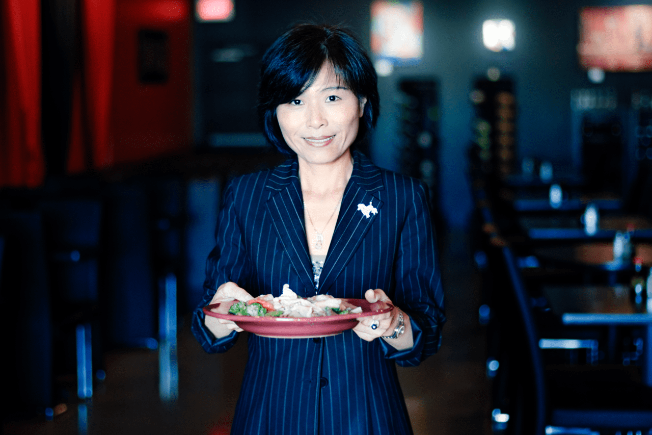 A woman in a black suit holding a plate of Asian food.