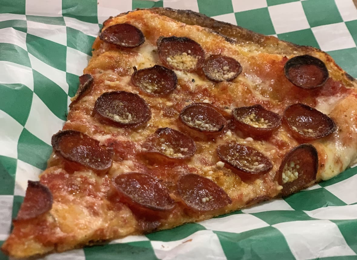 a slice of pepperoni pizza on a green and white checkered paper.