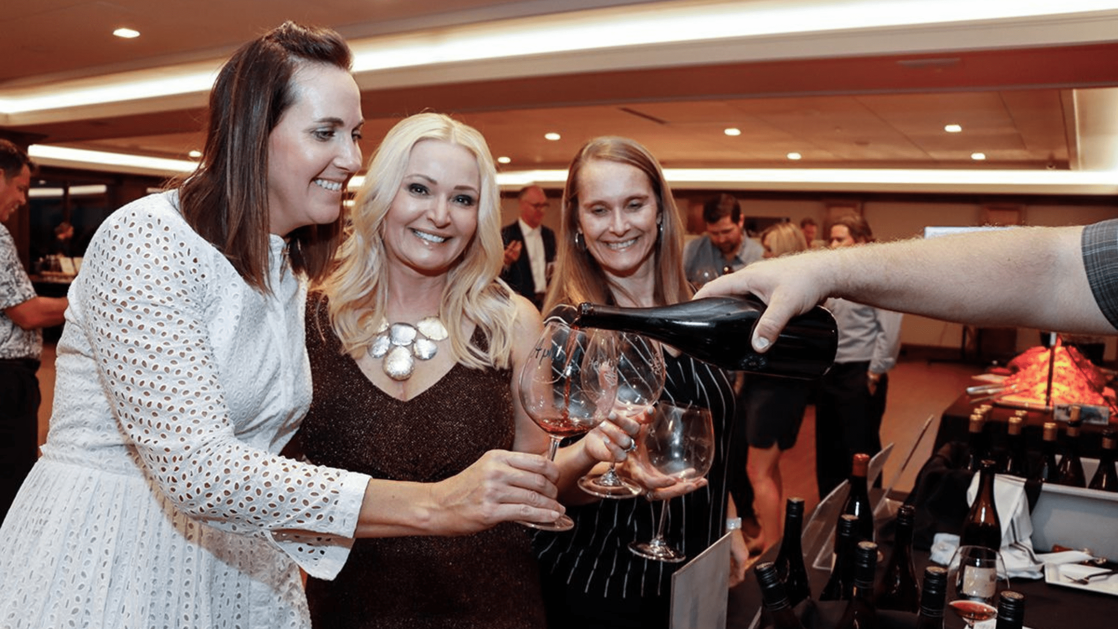 Guests enjoying wine tasting at Pinot, Pigs & Pours 2025 in Omaha, smiling while sampling red wine at a Completely KIDS charity event.