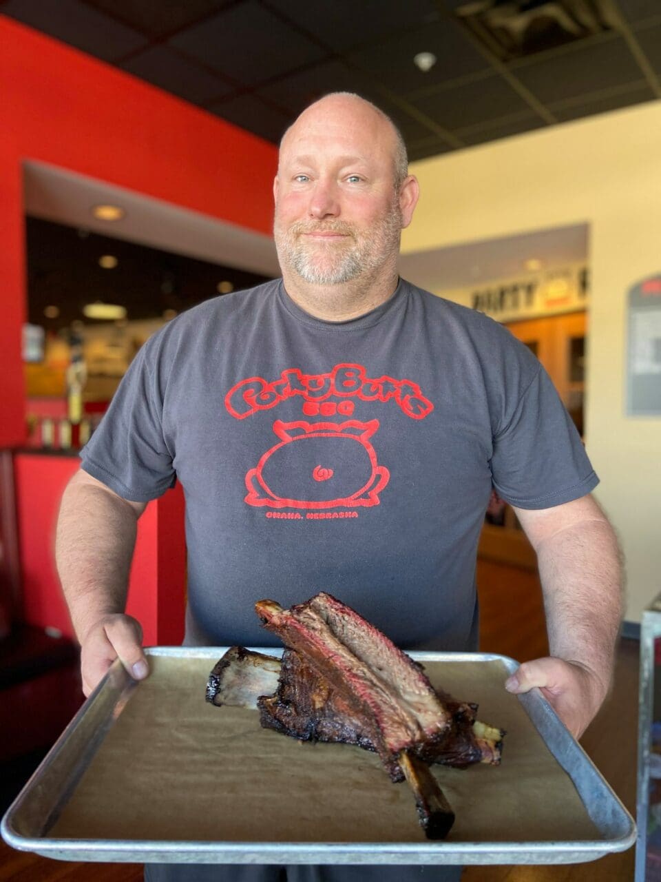 a handsome slightly overweight bald man holding two giant beef ribs. 