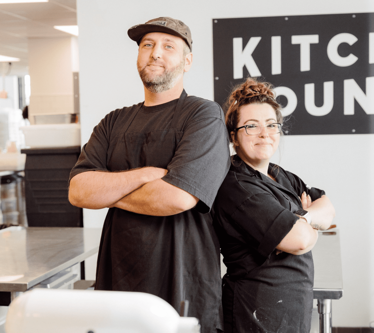 a male and a female vegan chefs standing with their arms crossed in a vegan bakery